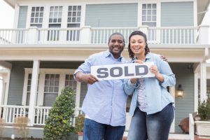 Couple Holding SOLD Sign in Front of House